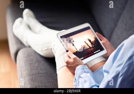 Woman watching tv series or movie stream with tablet on couch wearing cozy long socks. Girl streaming film with mobile device and on demand video.