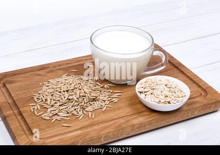 Oatmeal milk with oat seeds on wooden background. Vegetarian food Stock Photo
