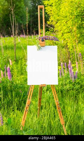 Wooden easel with white paper on green nature background Stock Photo
