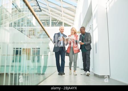 Group of business people looking at notebook and checking their business plans while walking along the office corridor Stock Photo