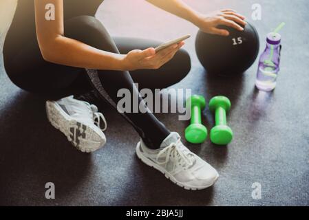 Woman using smartphone during workout at home in the living room. Online personal trainer or on mobile phone.Sport and recreation concept.advice to st Stock Photo