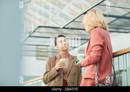 Two young businesswomen drinking coffee and talking to each other during coffee break Stock Photo