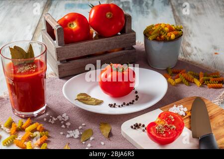 Ripe, fresh tomatoes, salt, pepper and basil with tomato juice and pasta Stock Photo
