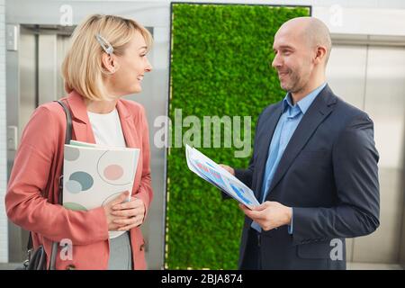 Business people holding reports and discussing them before business meeting while standing at office corridor Stock Photo