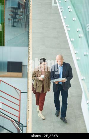 Businessman showing the document to his colleague and they discussing it while walking along the office corridor Stock Photo
