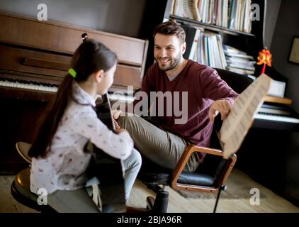 Cute little girl playing guitar with her music teacher in the rustic apartment Stock Photo