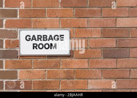 A bi-chromatic brick wall with a black and white Garbage Room sign Stock Photo