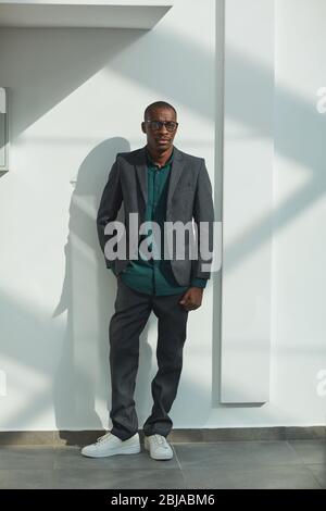 Portrait of African businessman in stylish suit looking at camera while standing against the white wall Stock Photo