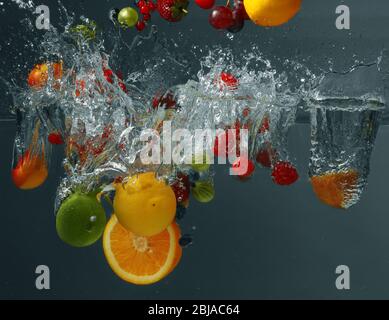 Different fruits and berries falling in water on dark background Stock Photo