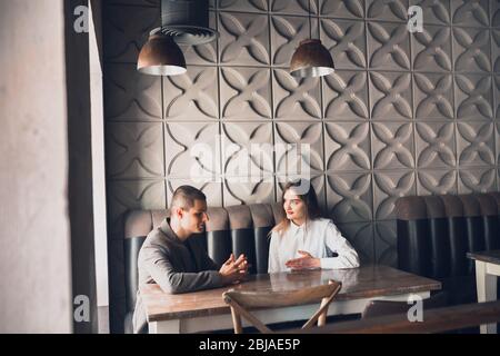 Cheerful man and woman talking, discussing at the coffee shop, cafe. Couple or friends, business partners working toghether, sitting at the table in casual attire. Communication, relations concept.
