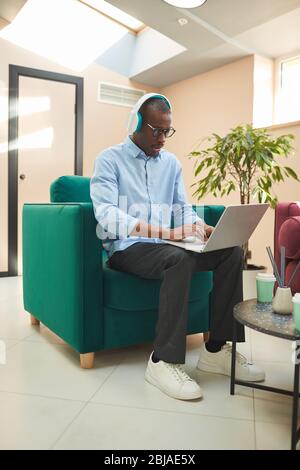Serious African businessman wearing headphones working online on his laptop at office Stock Photo