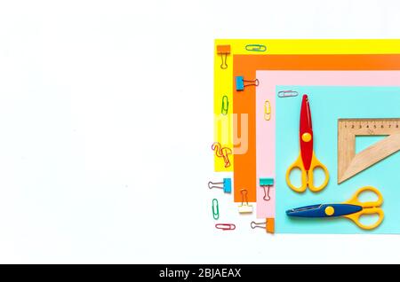 Sheets of colored paper arranged in a row, crayons, scissors and supplies on a white table. Children's art, Craft for kids or Preparing a child for sc Stock Photo