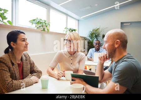 Group of business people sitting at the table drinking coffee and talking to each other during coffee break at office Stock Photo