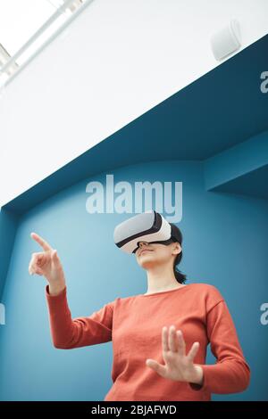Young woman wearing VR glasses gesturing while standing and playing in video games Stock Photo