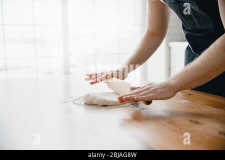 Hands of experienced chef man in apron preparing pizza dough on wooden table. Light background close-up Stock Photo