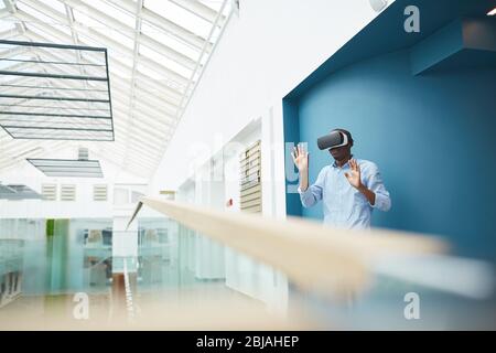 African businessman wearing virtual glasses standing and gesturing he talking to his colleague virtually at office Stock Photo