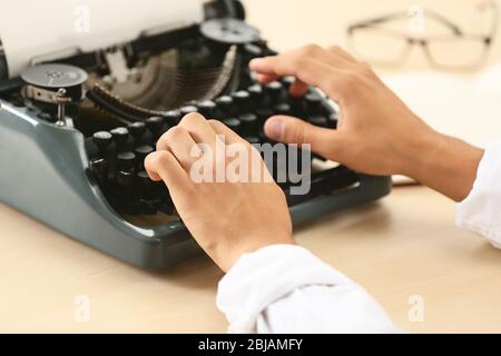 Man working on retro typewriter at desk Stock Photo