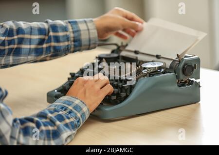 Man working on retro typewriter at desk Stock Photo