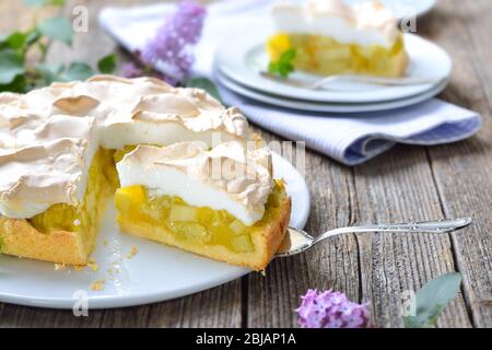 Delicious rhubarb cake topped with sweet meringue served on a wooden table with springlike lilac decoration Stock Photo