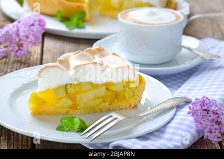 Delicious rhubarb cake topped with sweet meringue and a cup of cappuccino served on a wooden table with springlike lilac decoration Stock Photo