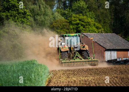 Farmer working the fields in spring, dry April 2020, tractor pulls thick cloud of dust, while cultivating, loosening the soil, behind him, Niederrhein