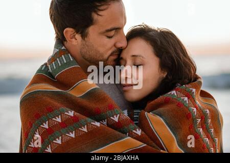 Affectionate young couple wrapped in a blanket at the beach Stock Photo