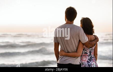Loving young couple looking out at the ocean at sunset Stock Photo