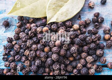 Black pepper and bay leaves are scattered on blue boards. Black pepper spices and seasonings for cooking. Stock Photo
