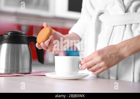 Woman having breakfast with cup of coffee and biscuit in kitchen Stock Photo