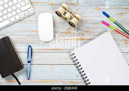 Office desktop with binoculars, keyboard, mouse, colored pens, diary and a white notebook on a top view concept Stock Photo