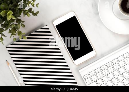 Close up on a white marble office desk with notebook, mobile, keyboard, mouse and a green plant Stock Photo