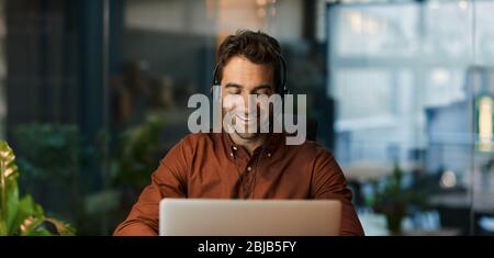 Smiling businessman talking on a headset and using a laptop Stock Photo