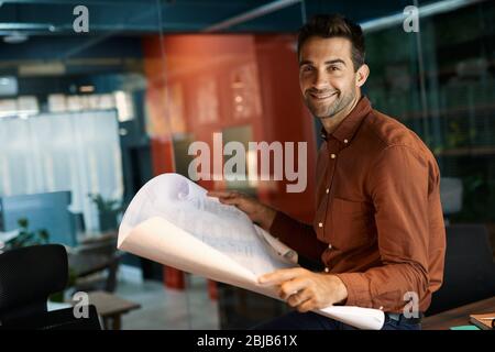 Smiling architect reading blueprints while working late in an office Stock Photo