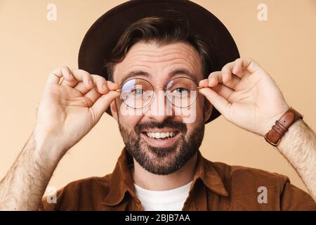 Image of optimistic surprised young unshaved man in hat isolated over beige wall background. Stock Photo