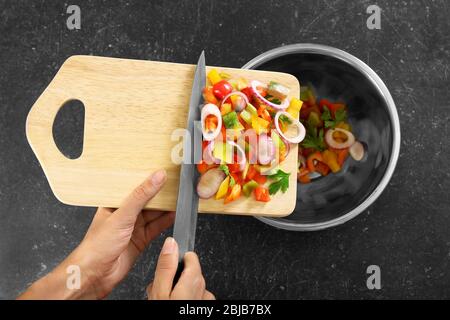 Woman putting chopped bell pepper with onion in bowl, top view Stock Photo