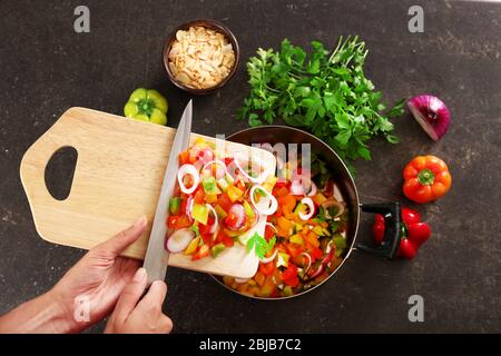 Woman putting chopped bell pepper with onion in saucepan, top view Stock Photo