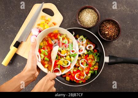 Woman putting chopped bell pepper with onion in pan, top view Stock Photo