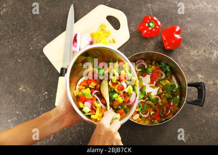 Woman putting chopped bell pepper with onion in saucepan, top view Stock Photo