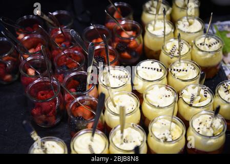 Fruits and desserts in small little glass jars with spoons. Catering service concept - business event desserts laid out ready for service. Stock Photo