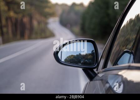 Car rear view mirror on wooded rural road Stock Photo