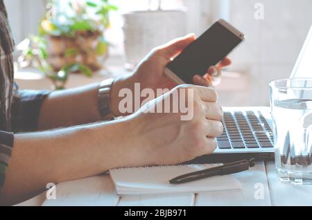 Businessman, freelancer holding pen, using mobile smart phone, working on laptop computer at home Stock Photo