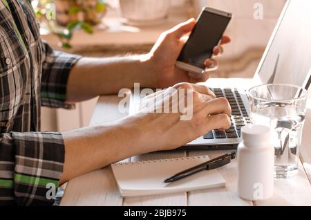 Businessman, freelancer holding pen, using mobile smart phone, working on laptop computer at home Stock Photo