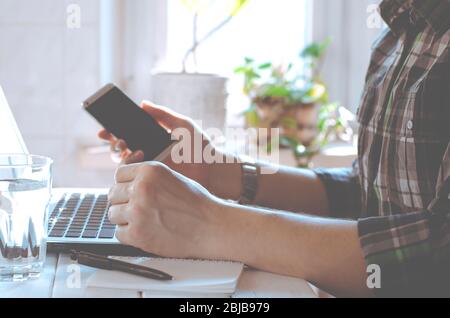Businessman, freelancer holding pen, using mobile smart phone, working on laptop computer at home Stock Photo