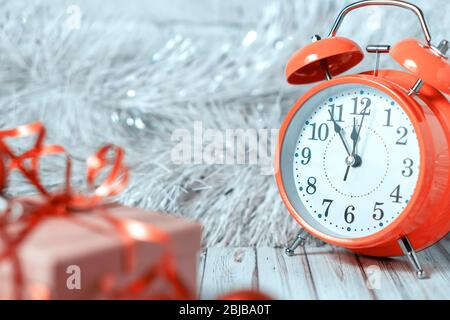 Gift box and blurred alarm clock on background on a wooden table decorated with a garland and red Christmas balls for the New Year or XMAS. Copy space Stock Photo