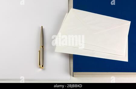 A book, three envelopes, an elegant pen and a small pile of white paper sheets on a wooden desk Stock Photo