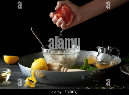 Female hand squeezing grapefruit juice in natural scrub on black background Stock Photo