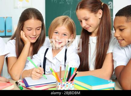 Schoolchildren drawing while sitting at table in classroom Stock Photo