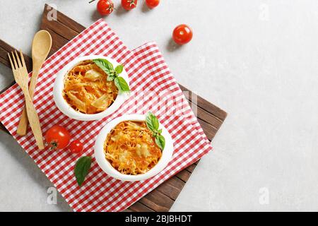 Portions of pasta Al Forno in ceramic bowls and red napkin on wooden board Stock Photo