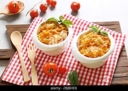 Portions of pasta Al Forno in ceramic bowls and red napkin on wooden board Stock Photo