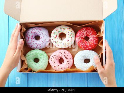Female hands holding box with colorful donuts on blue wooden background Stock Photo